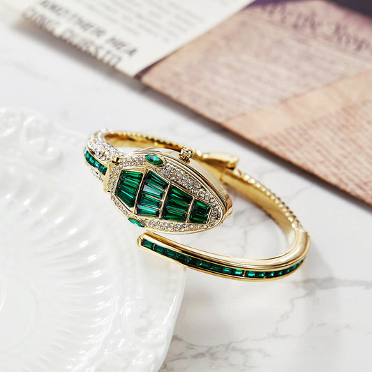 Gold snake watch with green baguette crystals on a marble tray