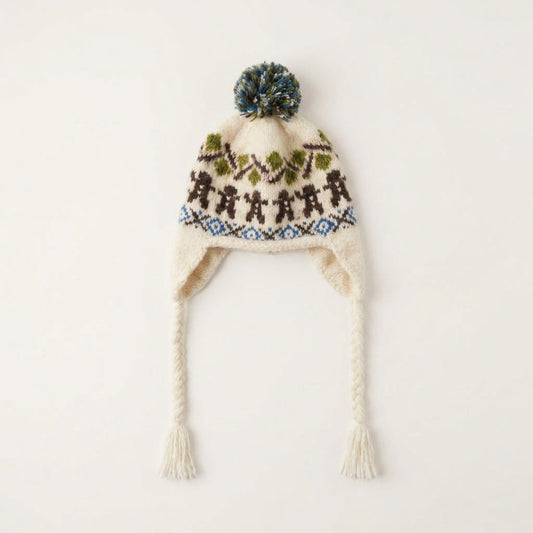 Cream gingerbread man ear-flap hat with green pom-pom and braided tassel ties, laid flat