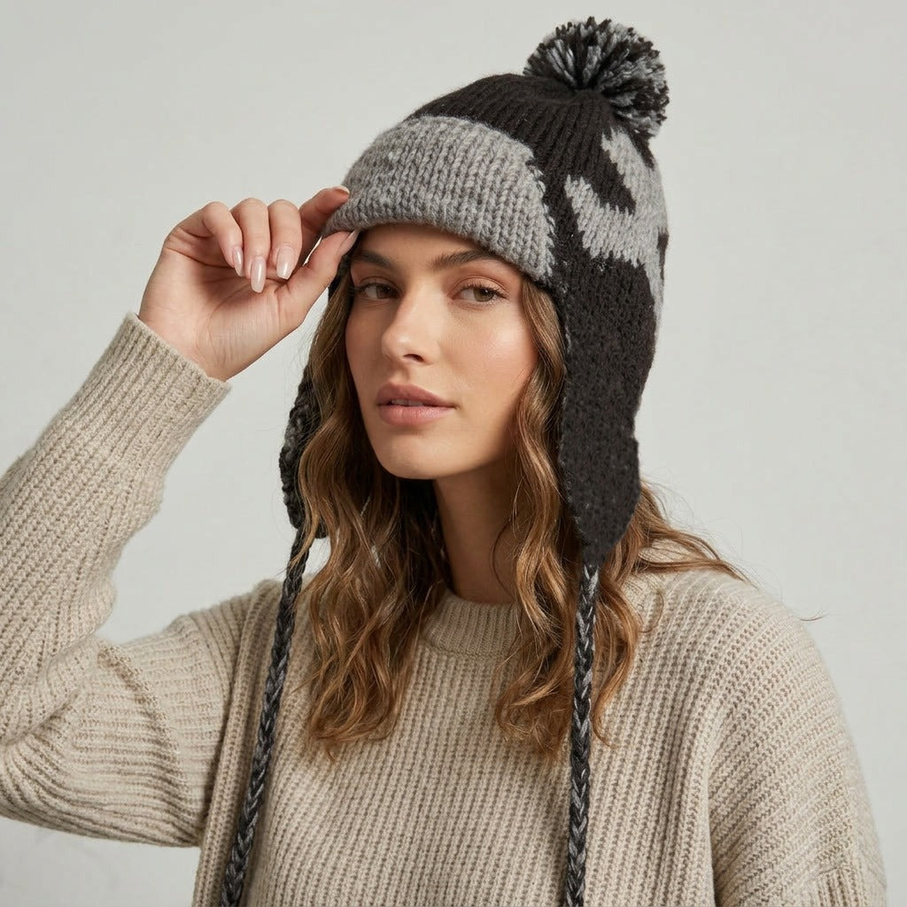 Woman touching the brim of the black and grey heart pattern ear-flap hat