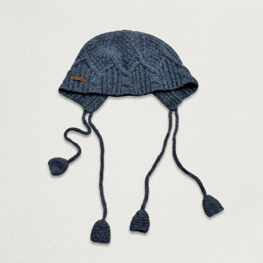 Blue cable-knit jellyfish hat with four dangling cords, laid flat