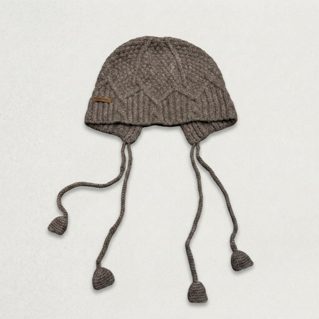 Grey cable-knit jellyfish hat with four dangling cords, laid flat