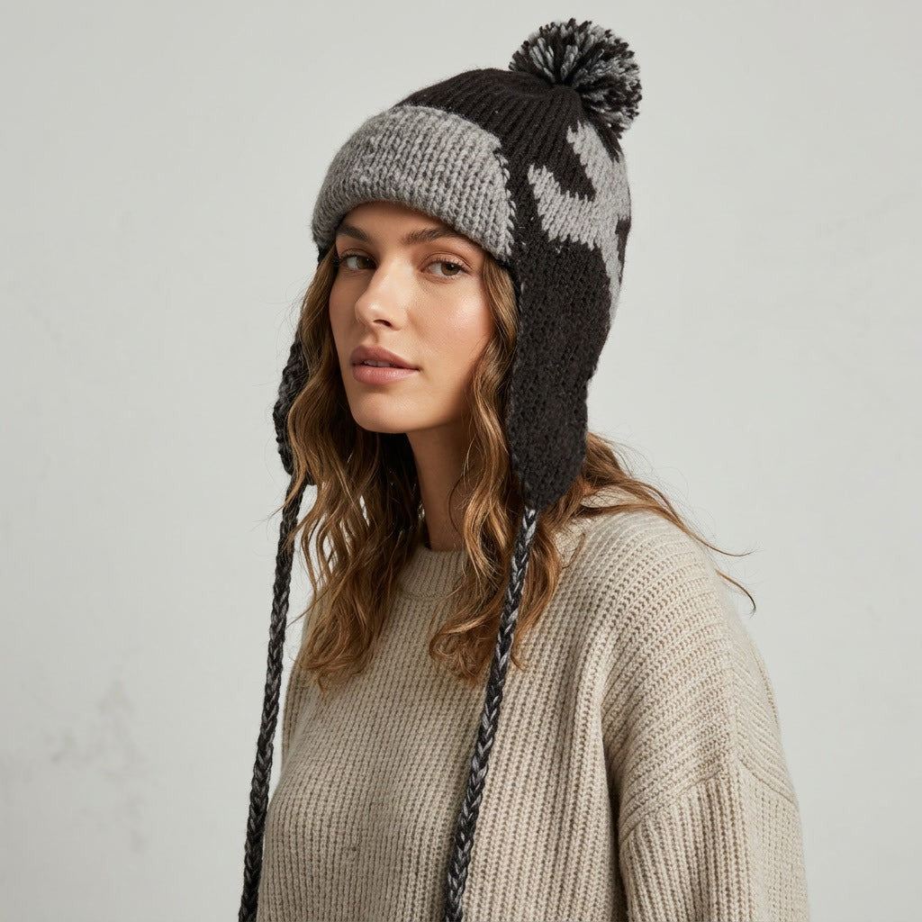 Side view of a woman wearing the black heart pattern ear-flap hat with pom-pom