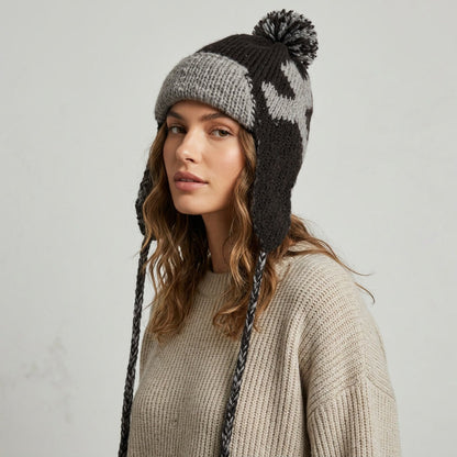 Side view of a woman wearing the black heart pattern ear-flap hat with pom-pom