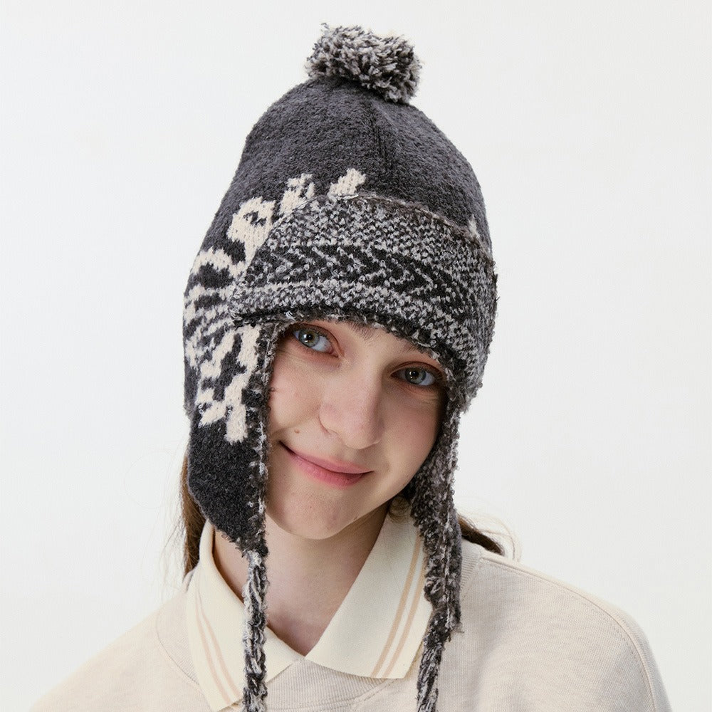 Close-up of the black trapper hat showing the patterned ear flaps and pom-pom