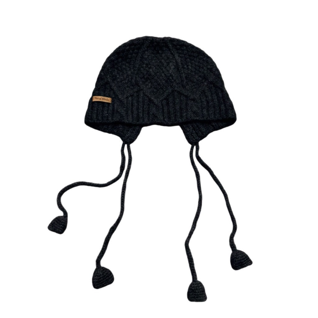 Black cable-knit jellyfish hat with dangling cords on a white background