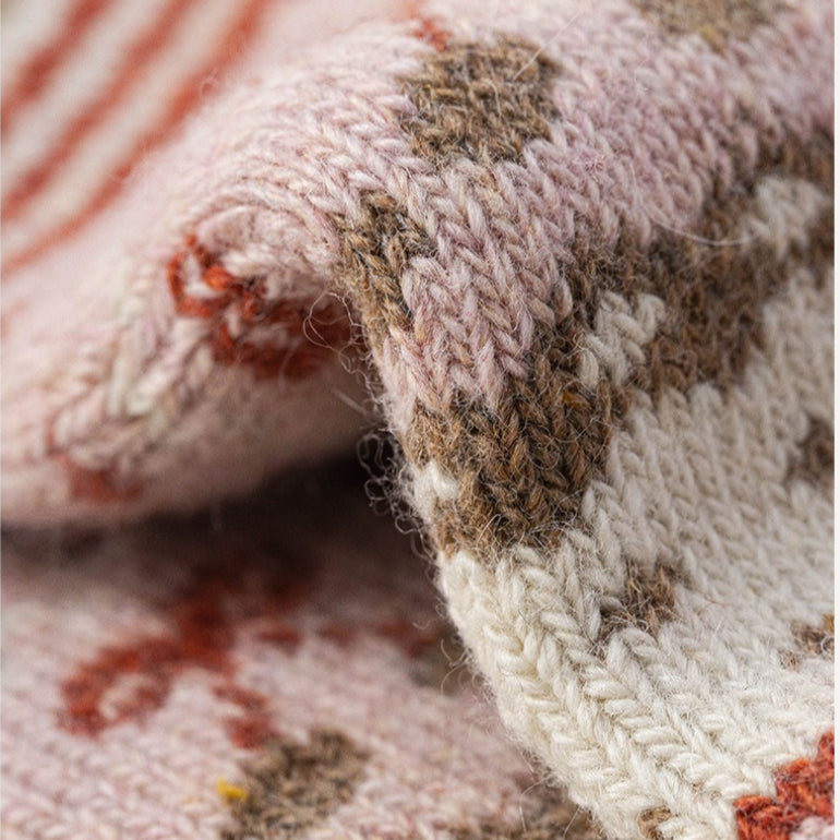 Close-up of soft pink Nordic woolen socks with brown, white, and orange traditional patterns.