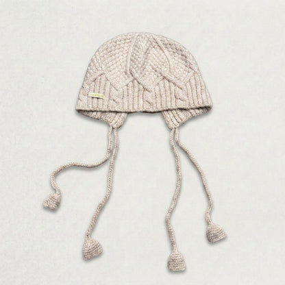Beige cable-knit jellyfish hat with four dangling cords, laid flat