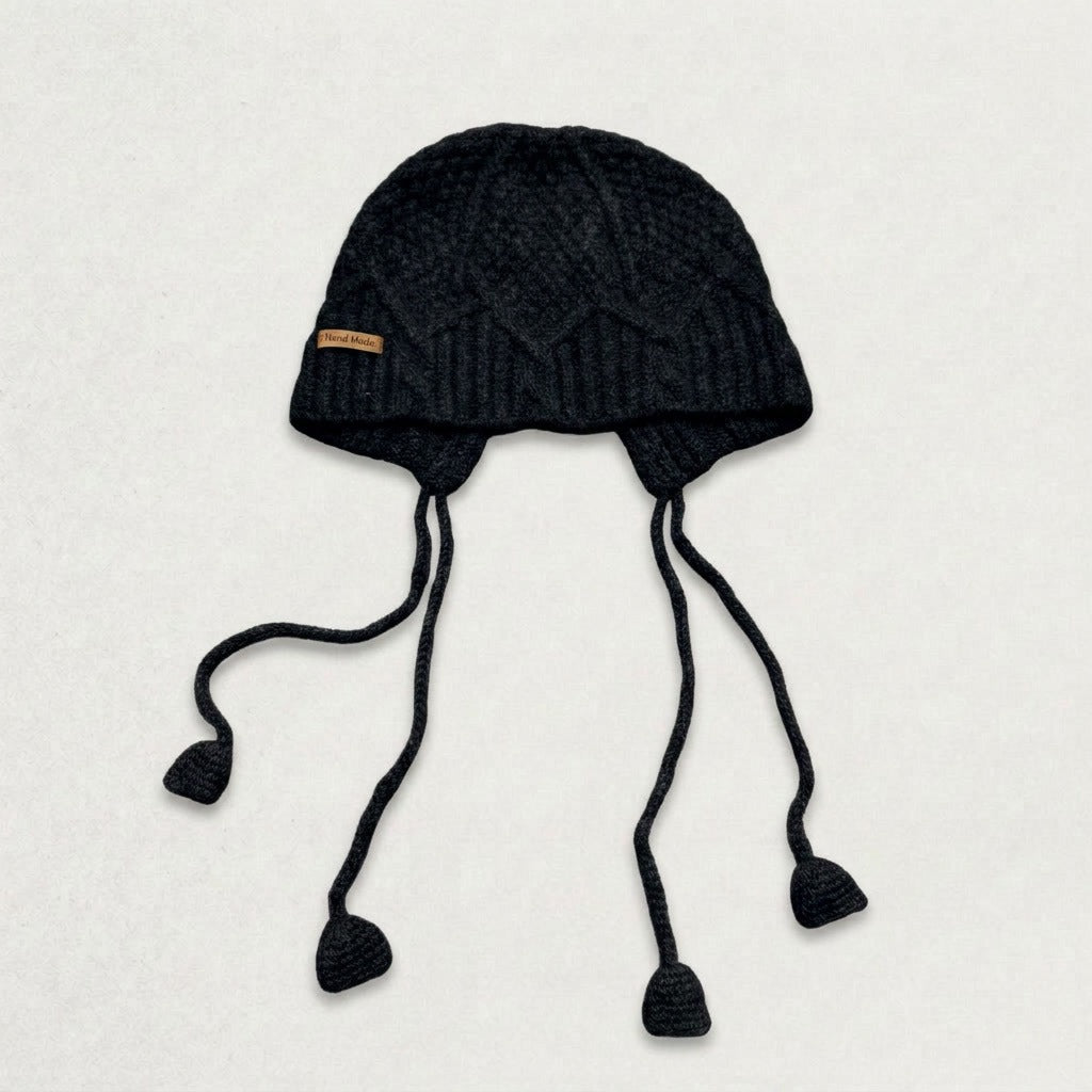 Black cable-knit jellyfish hat with four dangling cords, laid flat