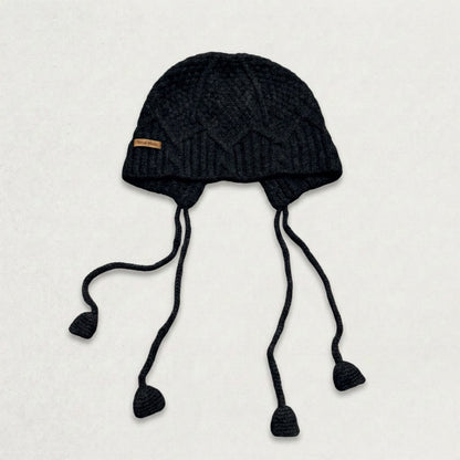 Black cable-knit jellyfish hat with four dangling cords, laid flat