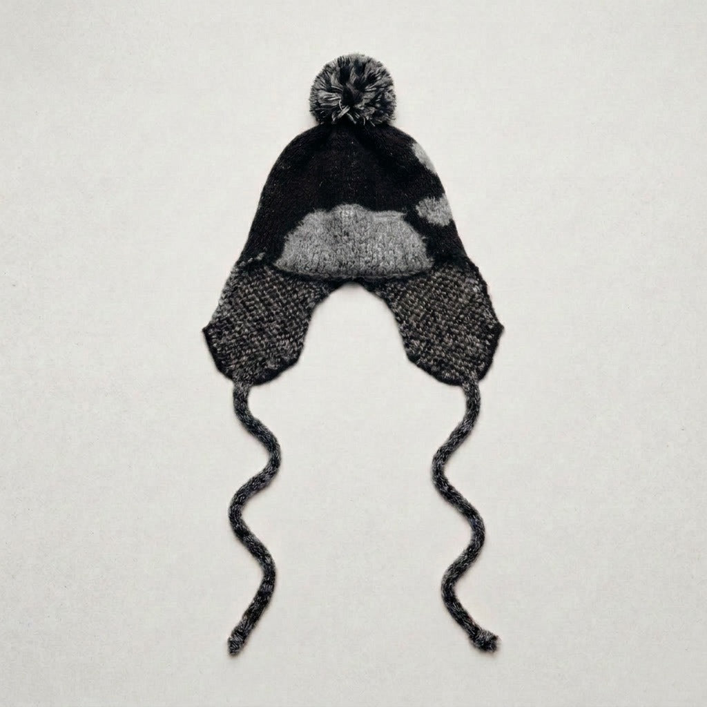 Black ear-flap hat with a grey heart pattern and twisted ties, laid flat