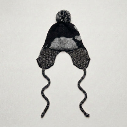 Black ear-flap hat with a grey heart pattern and twisted ties, laid flat