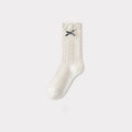 Cream cable knit crew sock with a black bow and subtle gray polka dots at the cuff.