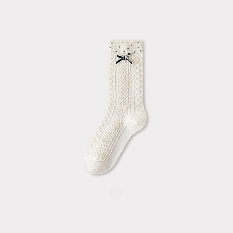 Cream cable knit crew sock with a black bow and subtle gray polka dots at the cuff.