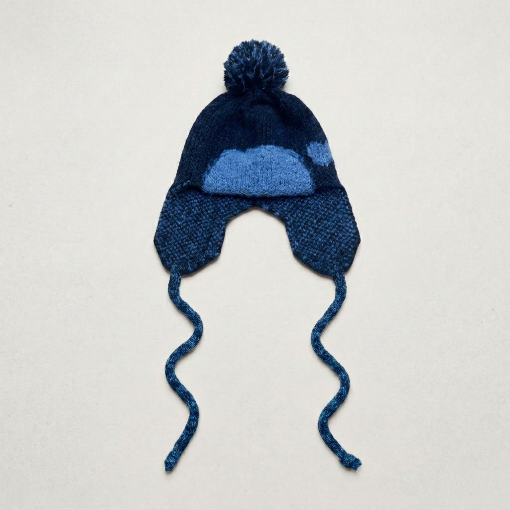 Navy ear-flap hat with a blue heart pattern, pom-pom and twisted ties, laid flat