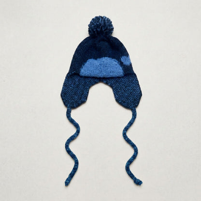 Navy ear-flap hat with a blue heart pattern, pom-pom and twisted ties, laid flat