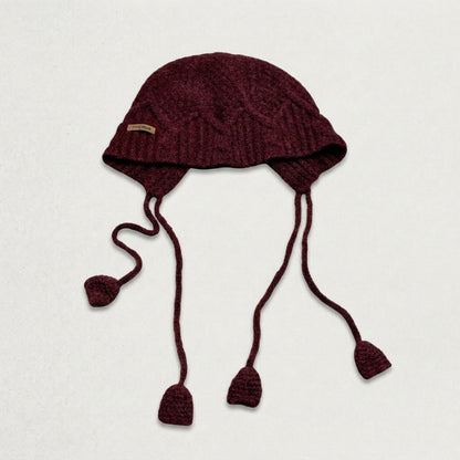 Burgundy cable-knit jellyfish hat with four dangling cords, laid flat
