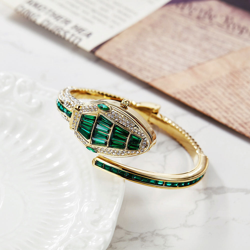 Gold snake watch with green baguette crystals on a marble tray