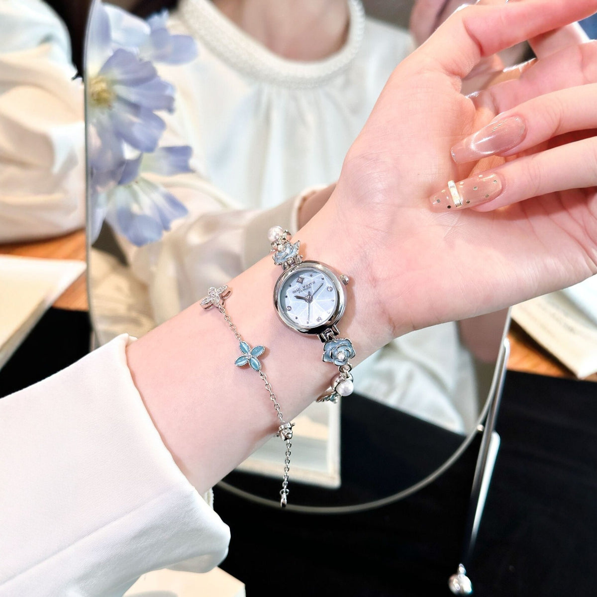 Silver camellia pearl bracelet watch with blue flowers worn on the wrist