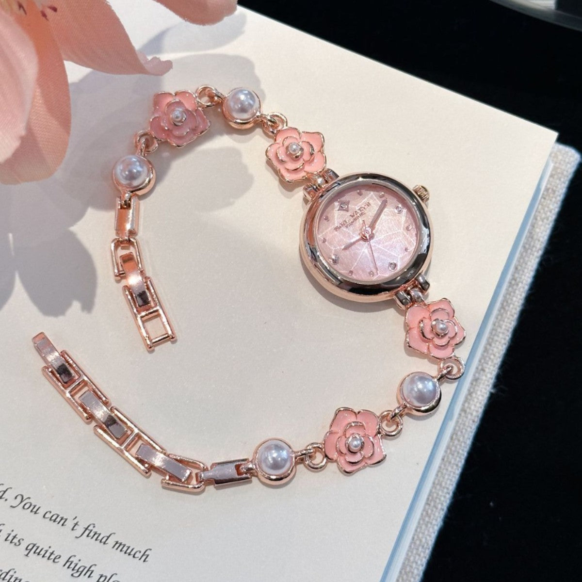 Rose gold camellia pearl bracelet watch with pink flowers on an open book