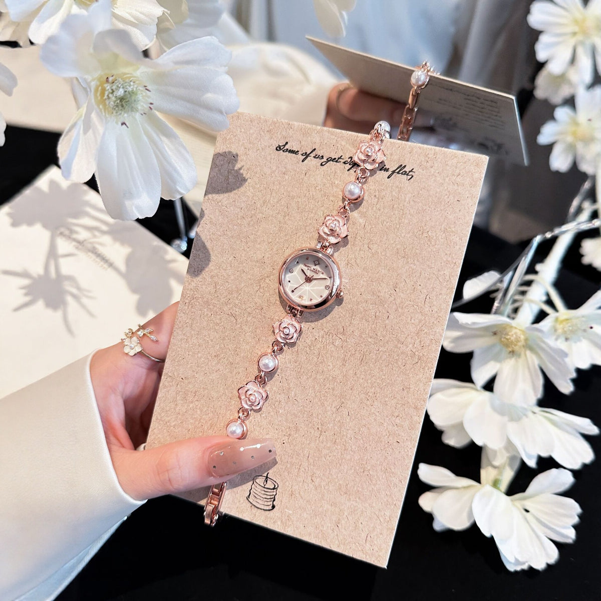 Rose gold camellia pearl bracelet watch on a card beside white flowers