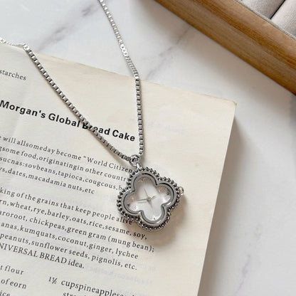 Silver clover necklace watch resting on an open book