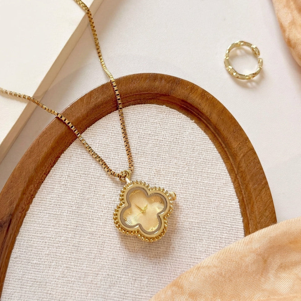 Gold clover necklace watch on a box chain beside a gold ring