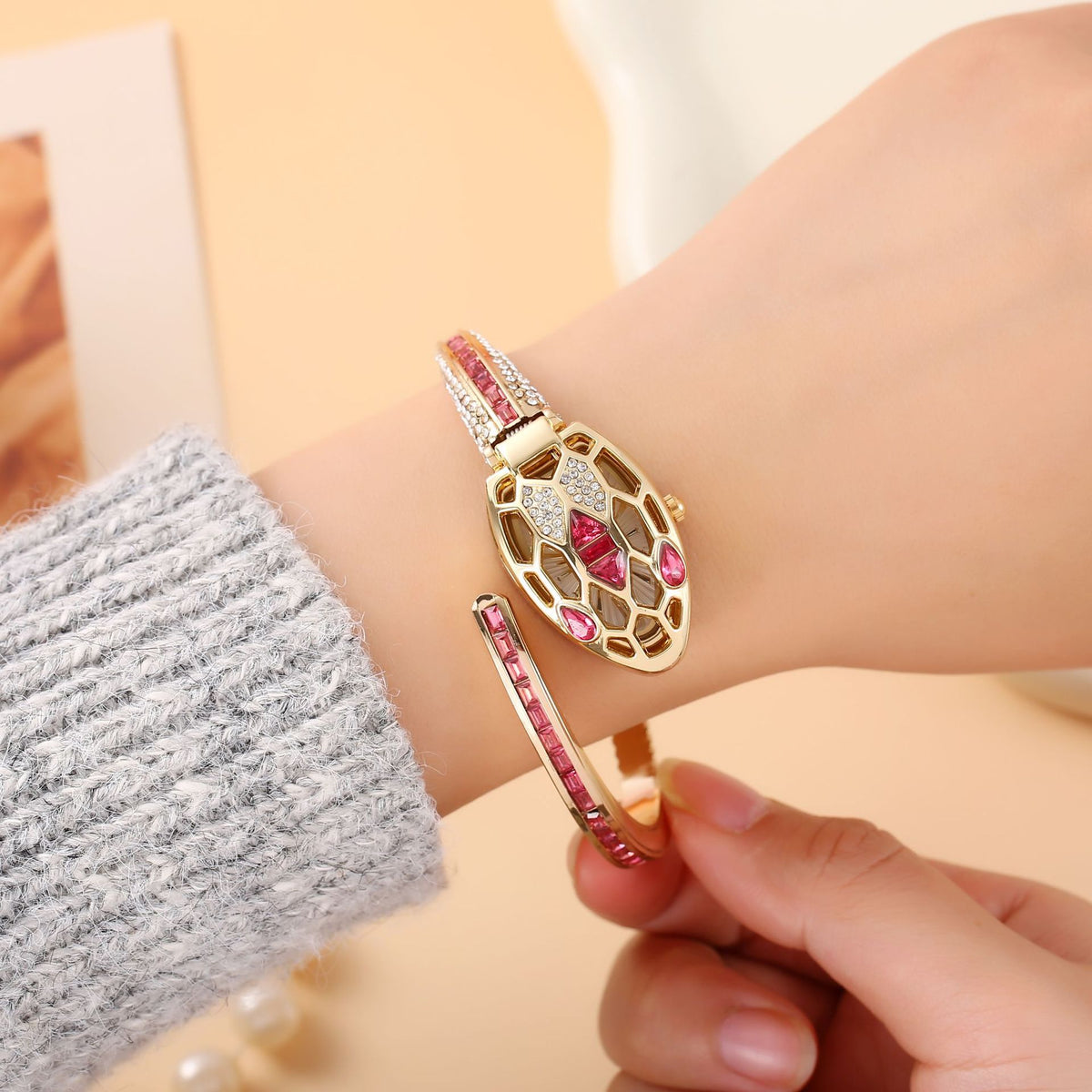 Gold snake bangle watch with red crystals on a woman's wrist
