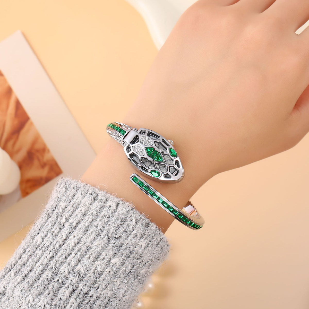 Silver snake bangle watch with green crystals worn on the wrist