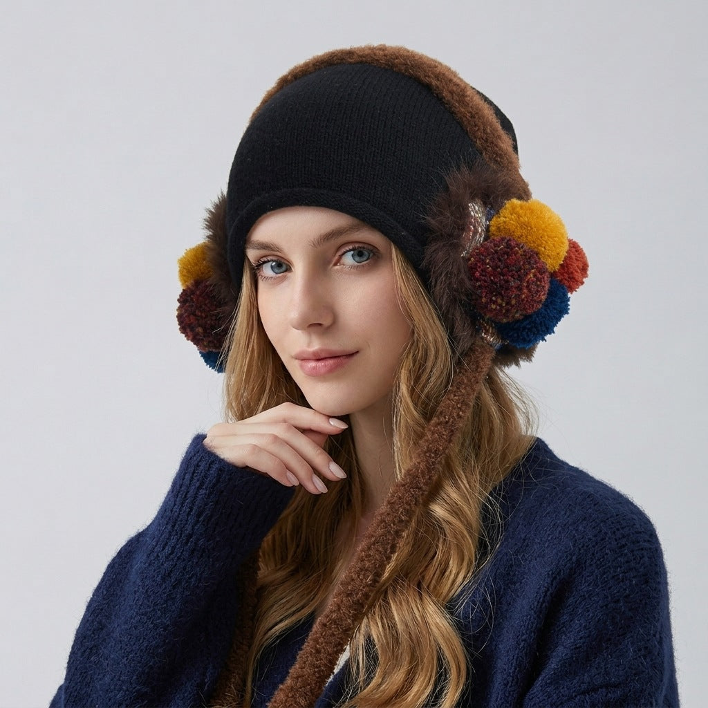 Woman wearing the black ear-flap hat with brown fluffy trim and multicoloured pom-poms