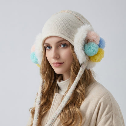 Woman wearing the white knitted ear-flap hat with pastel pom-pom clusters and a beige coat