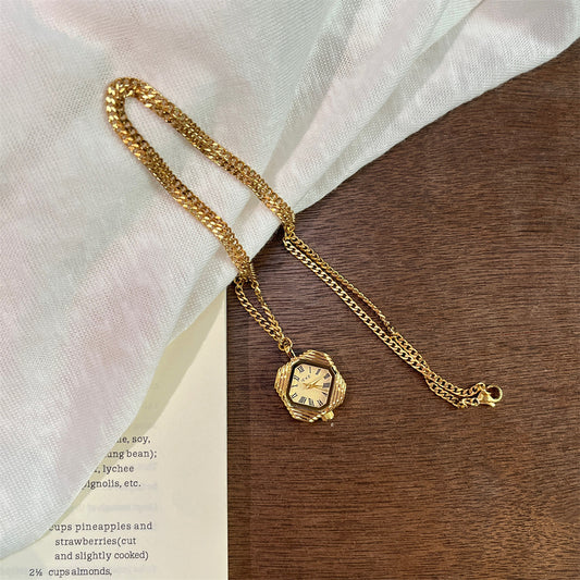 Gold octagon necklace watch with a gold dial lying on white linen