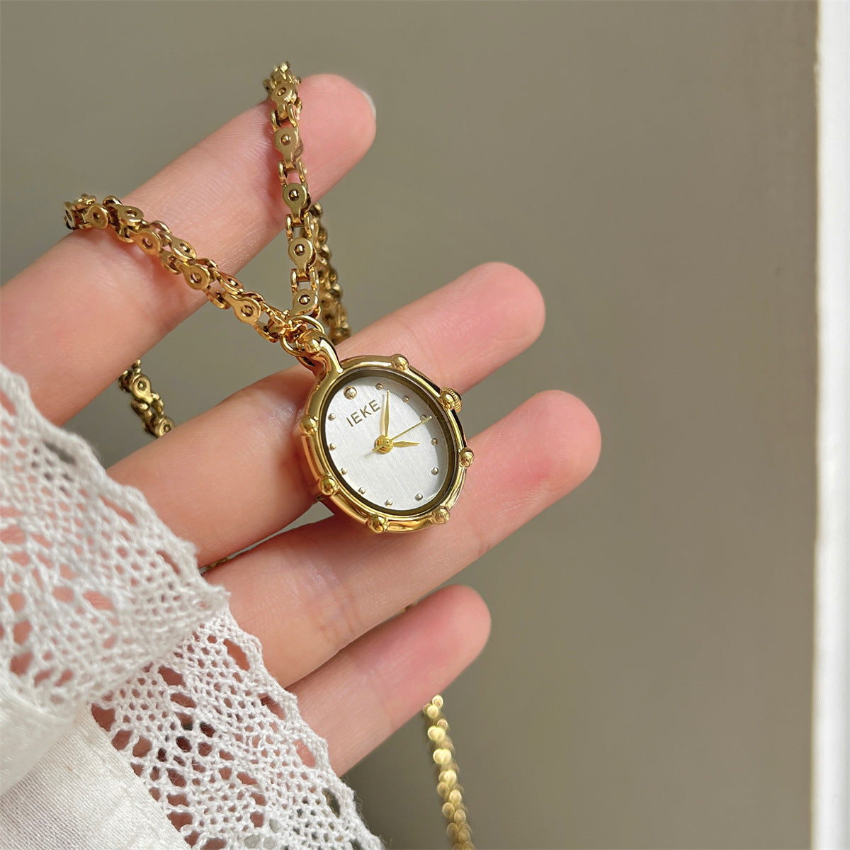 Hand holding a gold oval pendant watch with a white dial