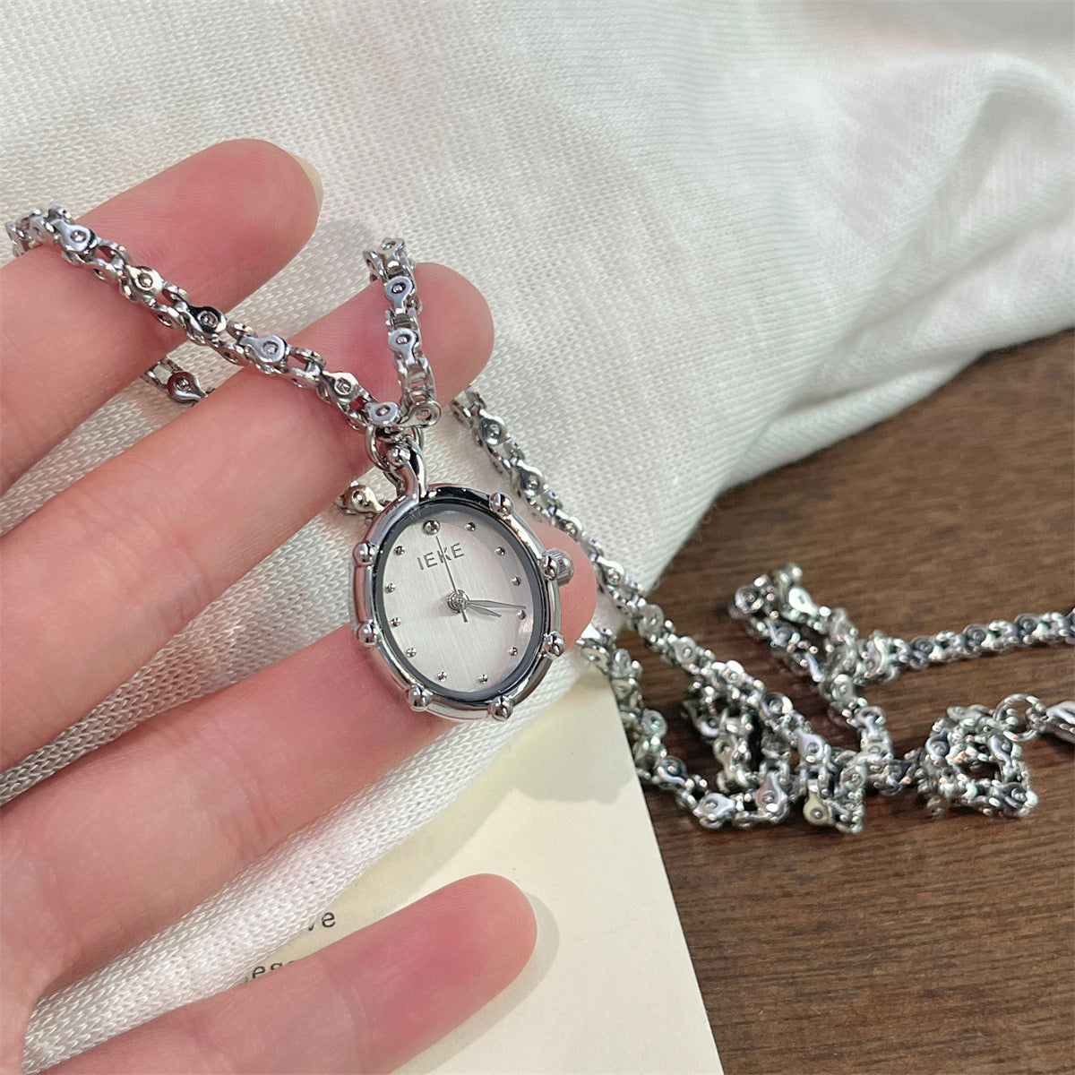 Hand holding a silver oval pendant watch with a white dial