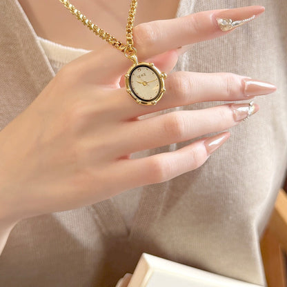 Hand holding a gold oval necklace watch with a beaded bezel