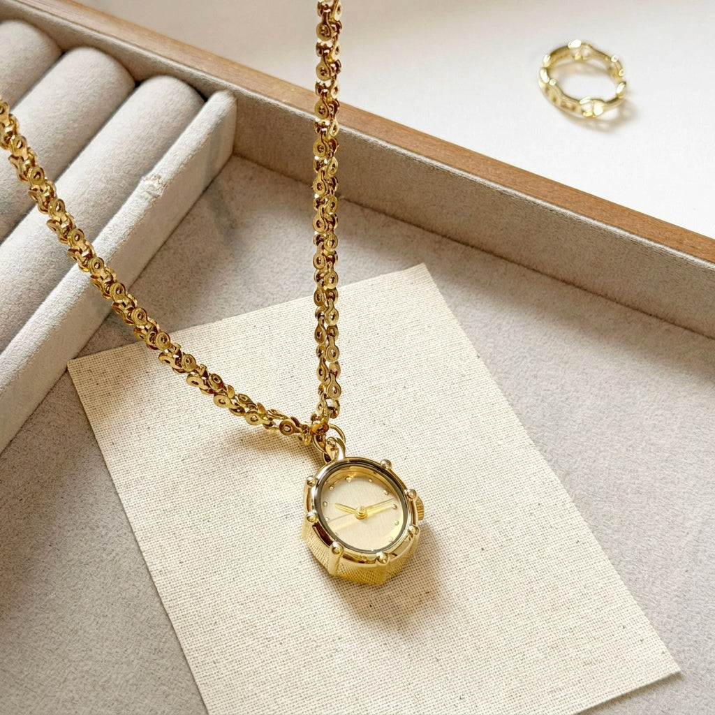 Gold oval pendant watch resting on a cream card with a gold ring