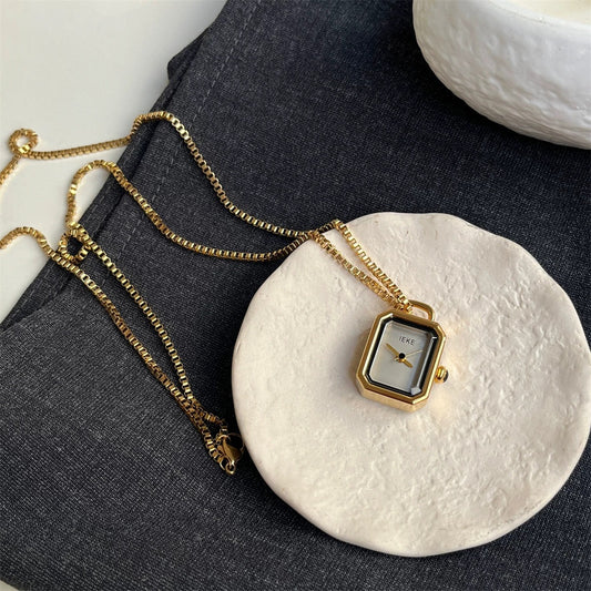 Gold rectangle pendant watch with a white dial on a ceramic dish