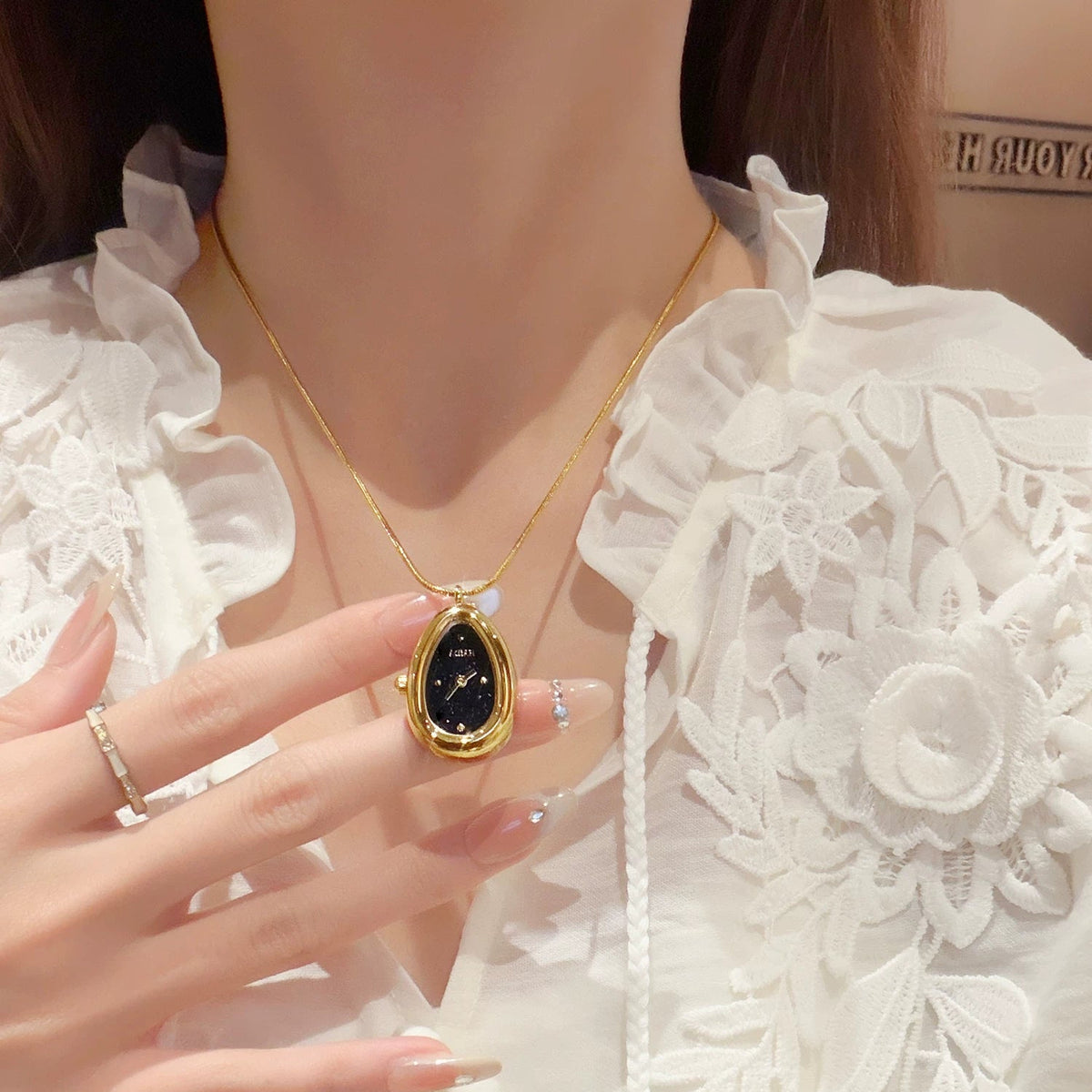 Close-up of a gold teardrop necklace watch with a white lace blouse
