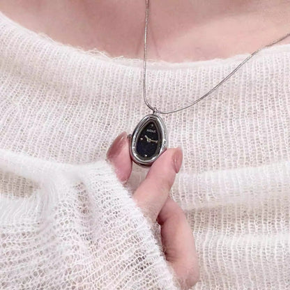 Woman wearing a silver teardrop necklace watch with a black dial over a white knit