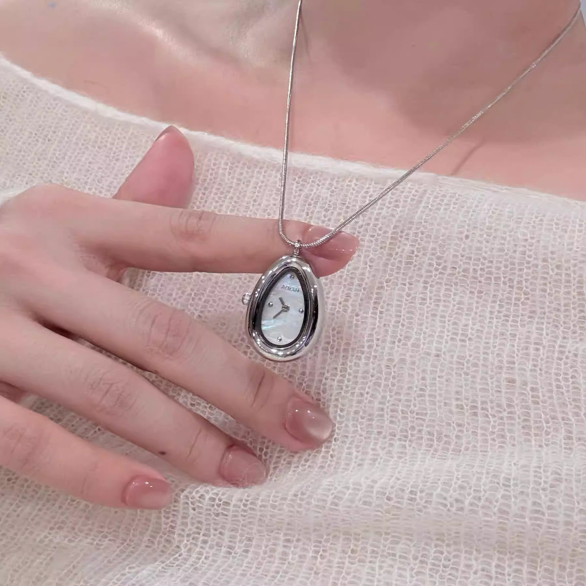 Hand holding a silver teardrop pendant watch with a black dial