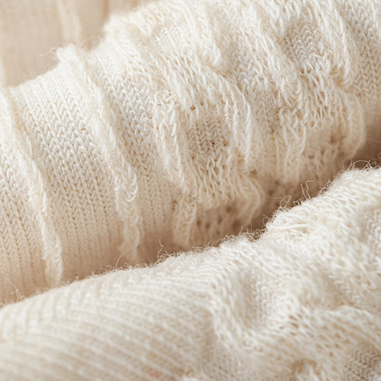 Close-up of a cream-colored, textured knit crew sock with subtle bow details.