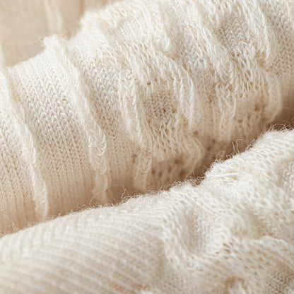 Close-up of a cream-colored, textured knit crew sock with subtle bow details.