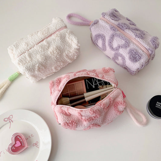 Fuzzy heart-pattern makeup bags in white, lilac and pink, one open with make-up inside